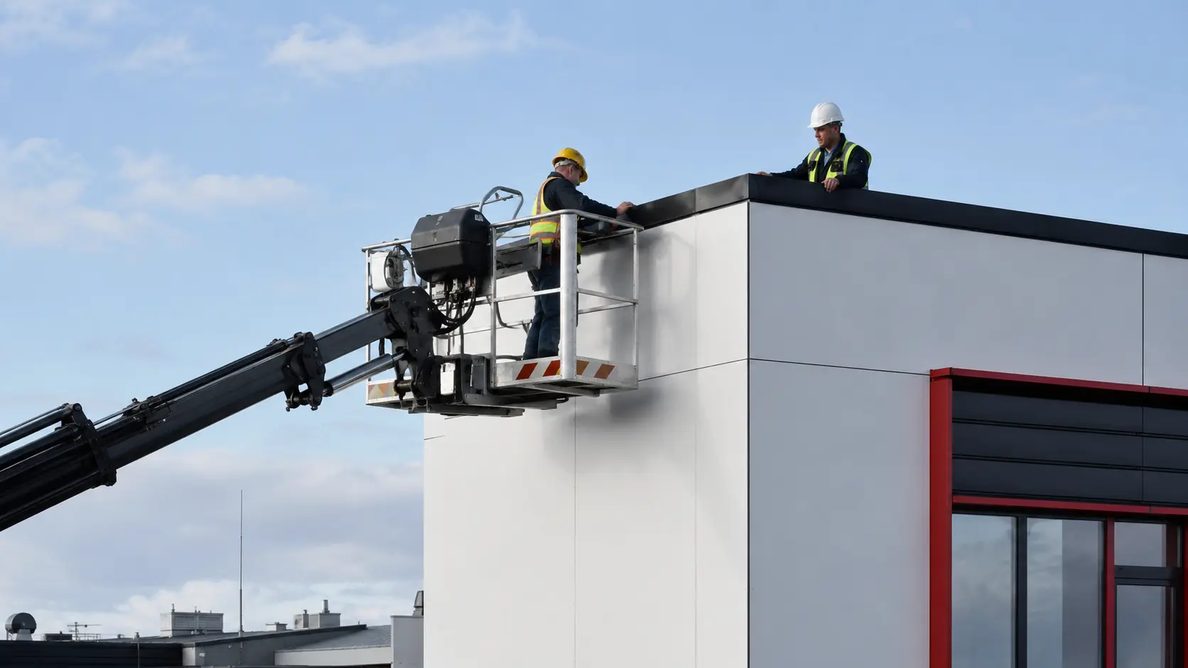 Arbeitsbühne mit gesichertem Monteur an der Dachkante eines Gewerbebaus