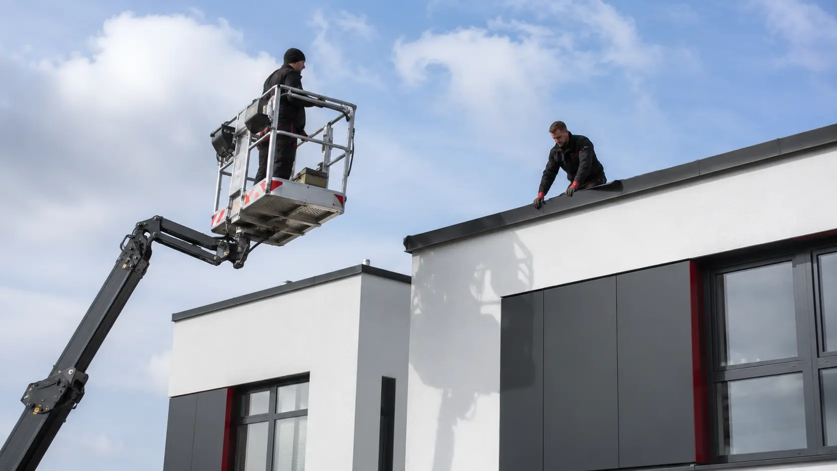 Monteur in der Arbeitsbühne arbeitet an der Attika eines Flachdachs